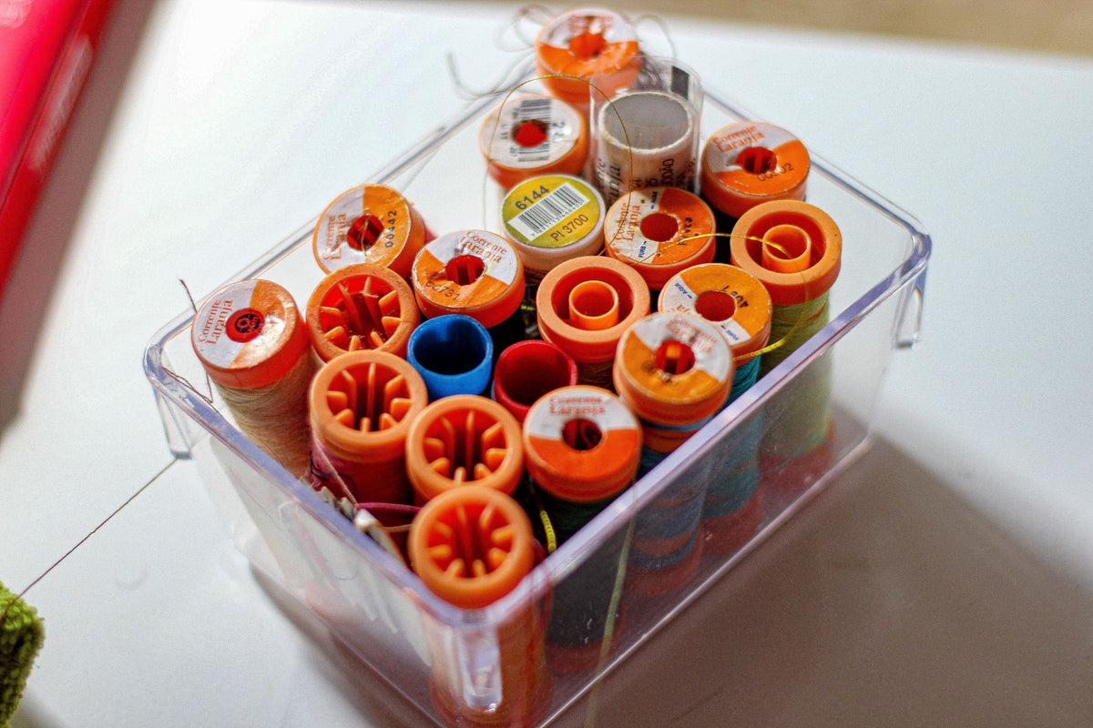 Close-up of assorted colorful thread spools stored neatly in a transparent container.