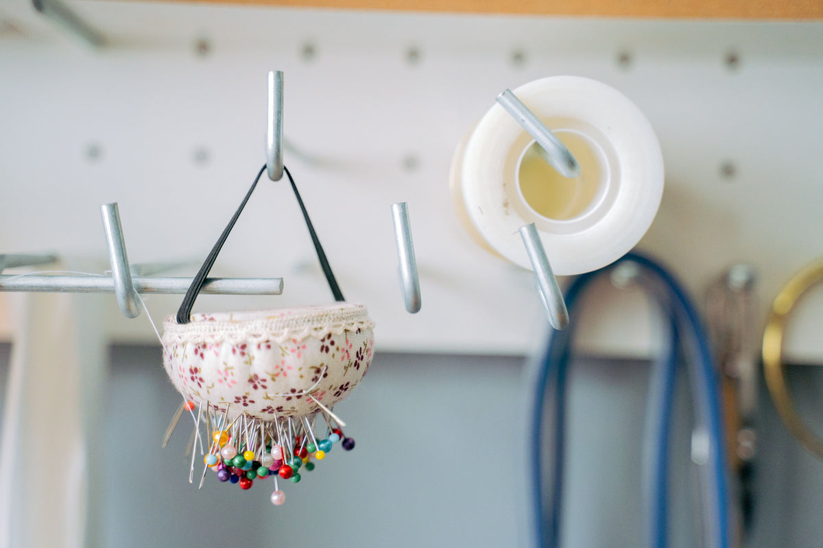Close-up of a pin cushion and tape hanging on hooks in a craft room.
