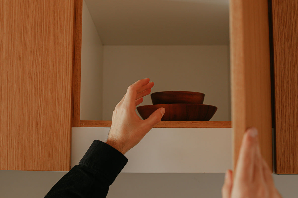 A person reaching into a wooden kitchen cabinet to retrieve stacked wooden bowls.